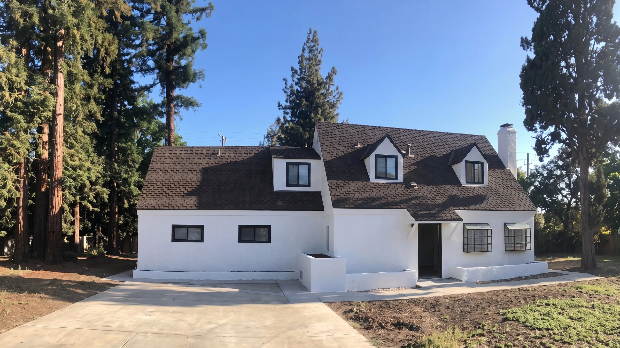A Central Valley home after a full exterior repaint: white stucco with black window trim, under mature redwoods.